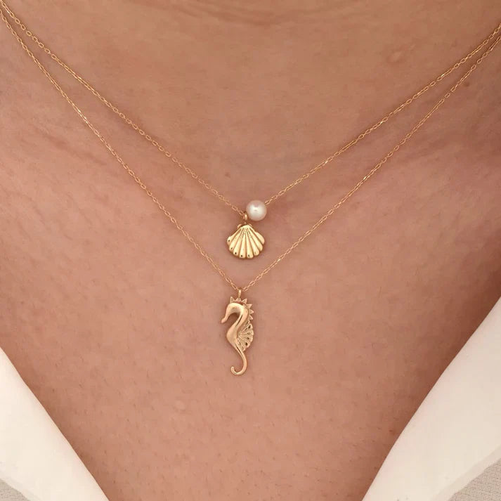 Gold necklace with seahorse and shell pendants on a person's neck