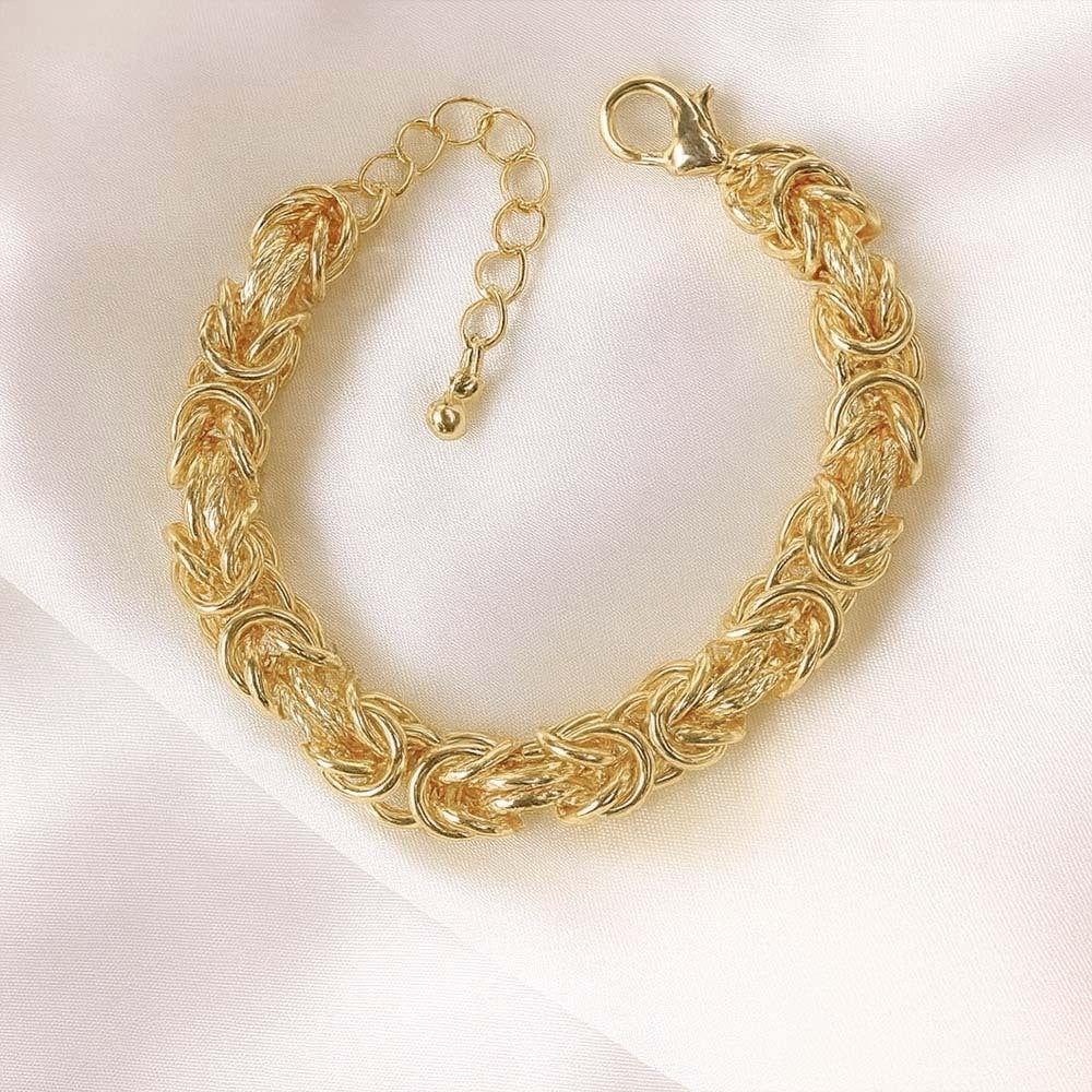 Detailed view of a gold  bracelet with textured chain links and an adjustable extension clasp on soft fabric