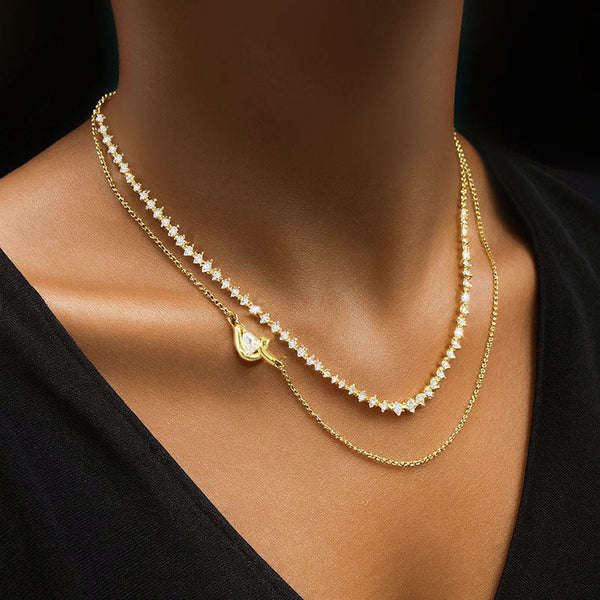 A two-layer gold necklace set featuring a pear-cut pendant on a fine chain, a row of white round-cut stones in the middle, and a simple gold chain as the base layer, styled on a model wearing a black V-neck top.