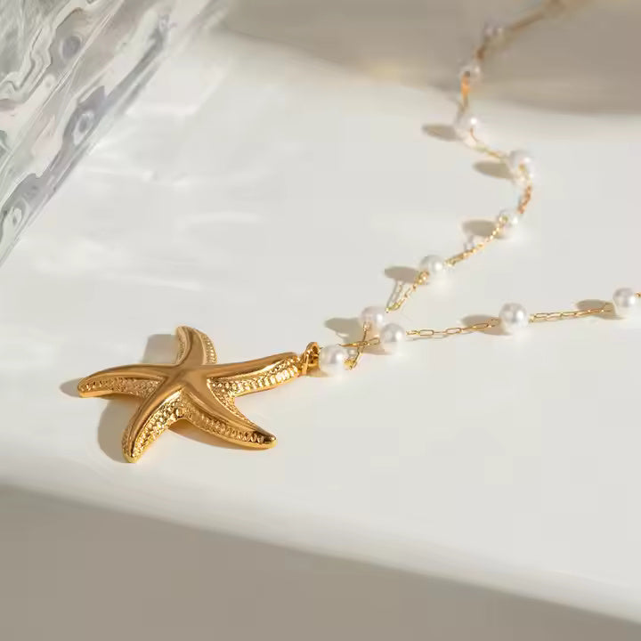 Gold starfish pendant necklace with pearls on a white surface