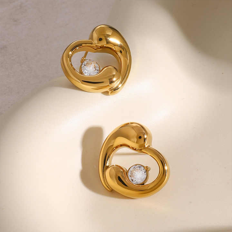 Gold heart-shaped earrings with embedded stones on a beige background