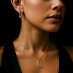 Close-up of a woman wearing a gold necklace and earring with gemstones.